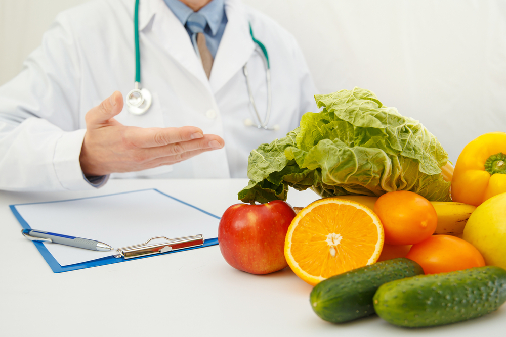 Médico apontando para frutas em cima da mesa.