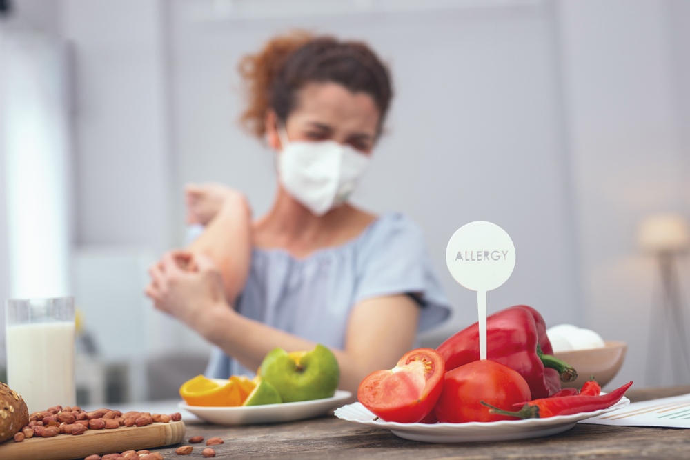 Mulher de máscara olhando para comidas em cima da mesa.